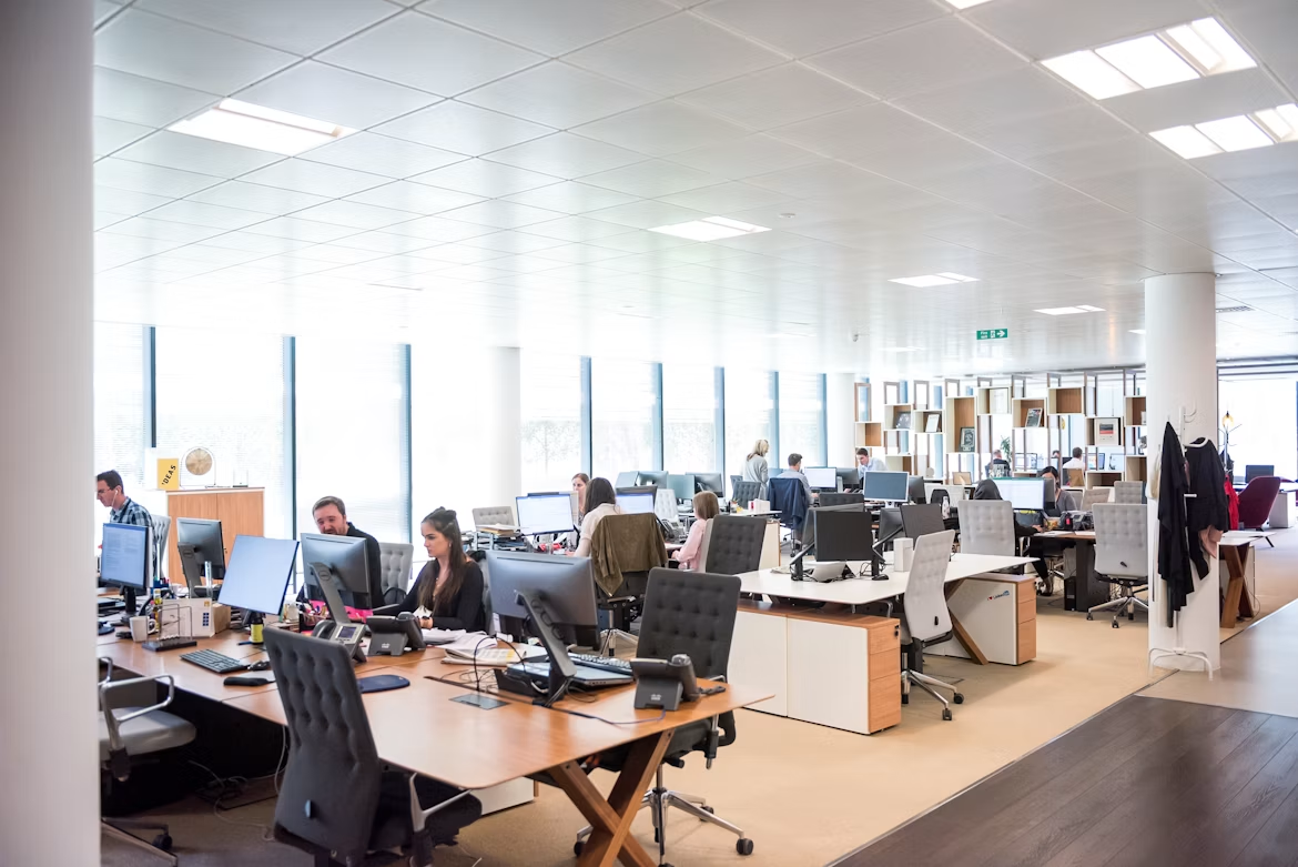 Bright open office with people working at desks and monitors